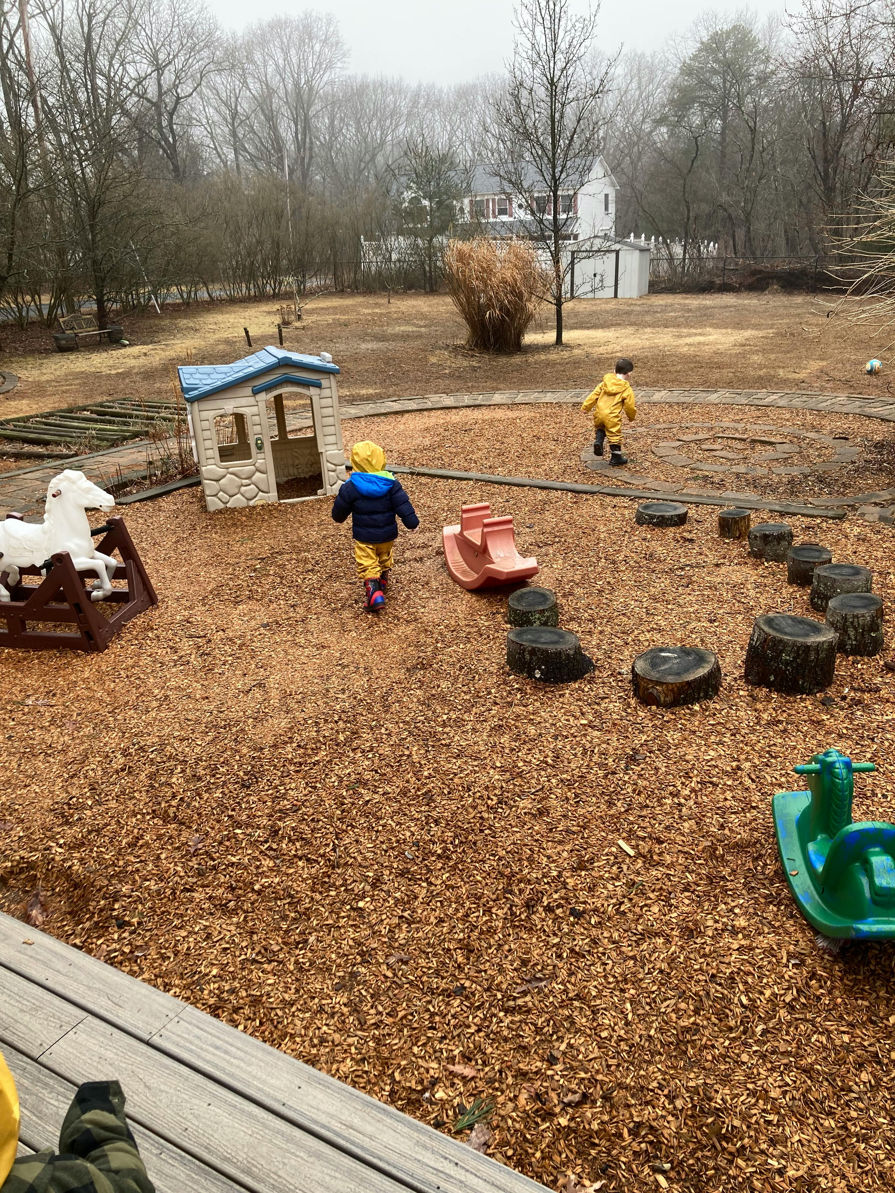 Two children walking on a playground with wood chips