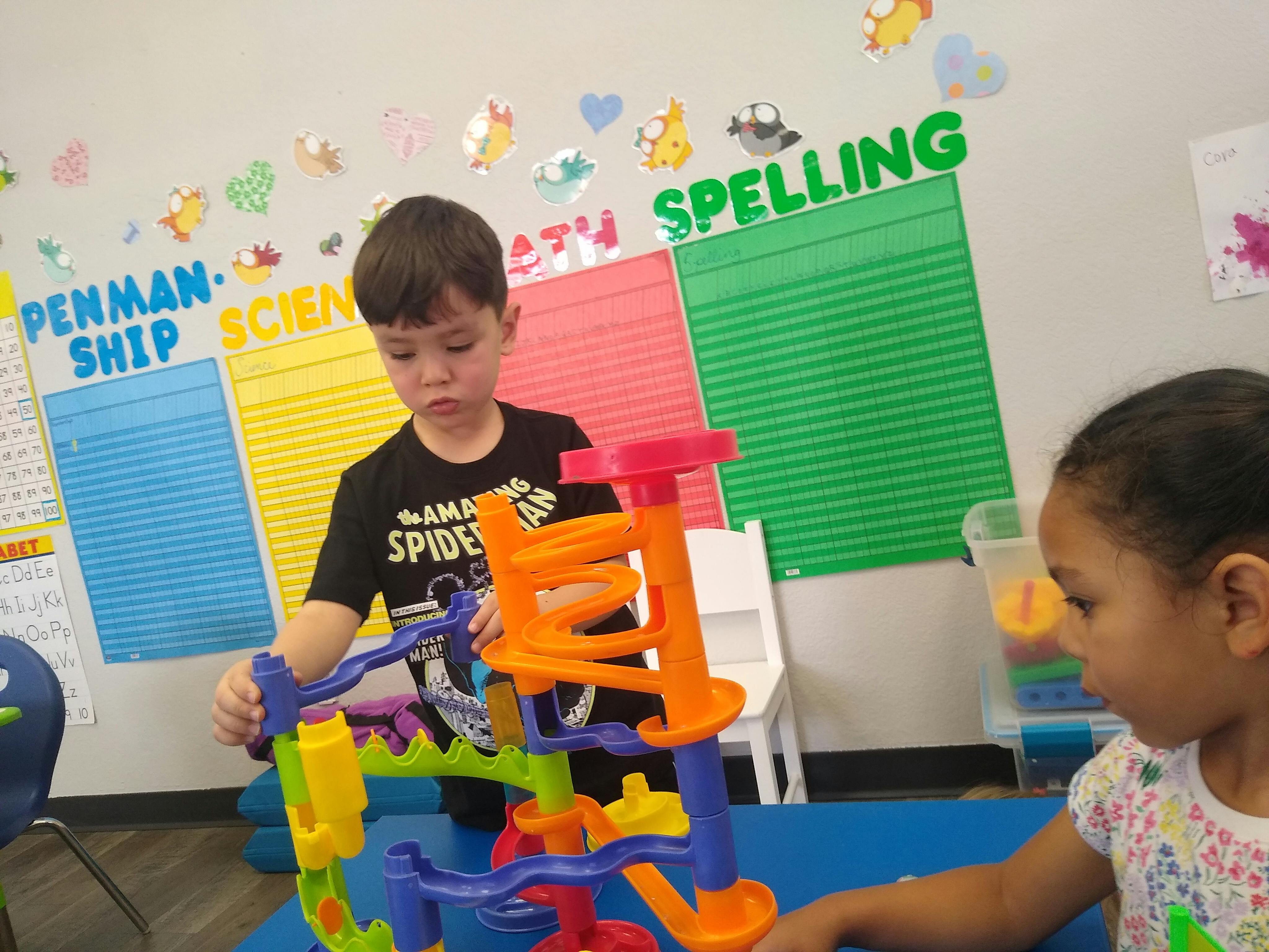 Two children playing with a colorful plastic marble run in a classroom
