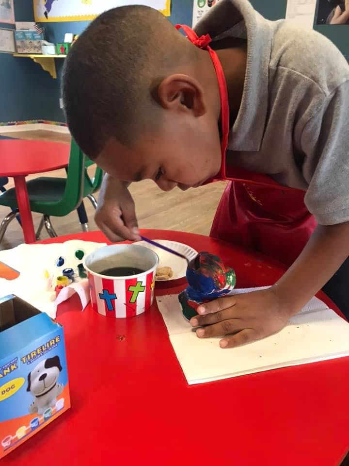 Child painting a small figurine at a red table