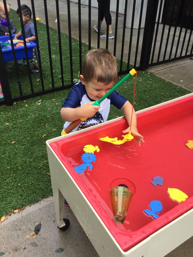 Child playing with a toy fishing rod in a water table