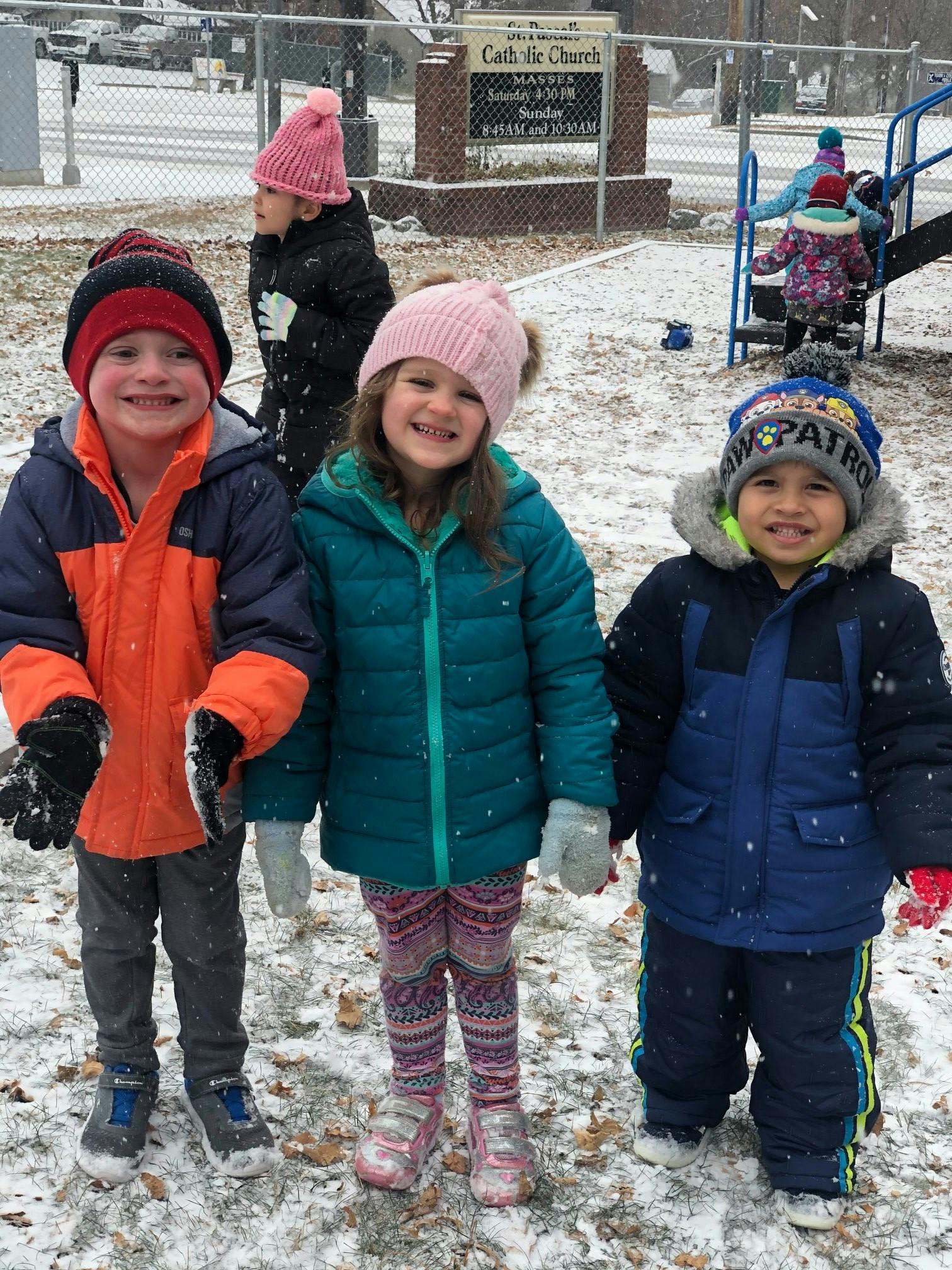 Three children in winter coats and hats standing in snow