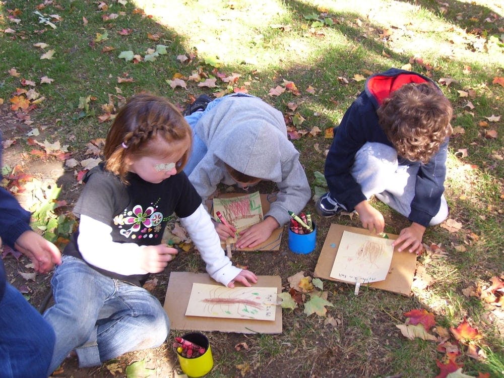 Three children drawing on paper outdoors