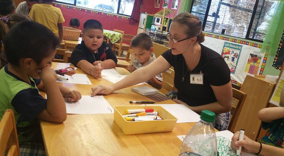 Adult and children drawing at a table in a classroom