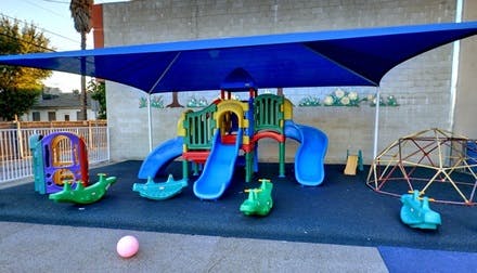 Playground with slides, climbing dome, and spring riders under a blue shade