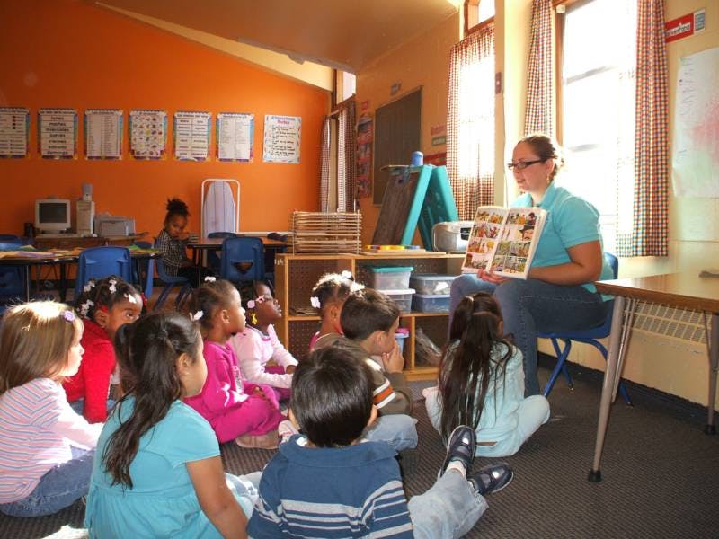 Person reading a book to a group of children in a classroom