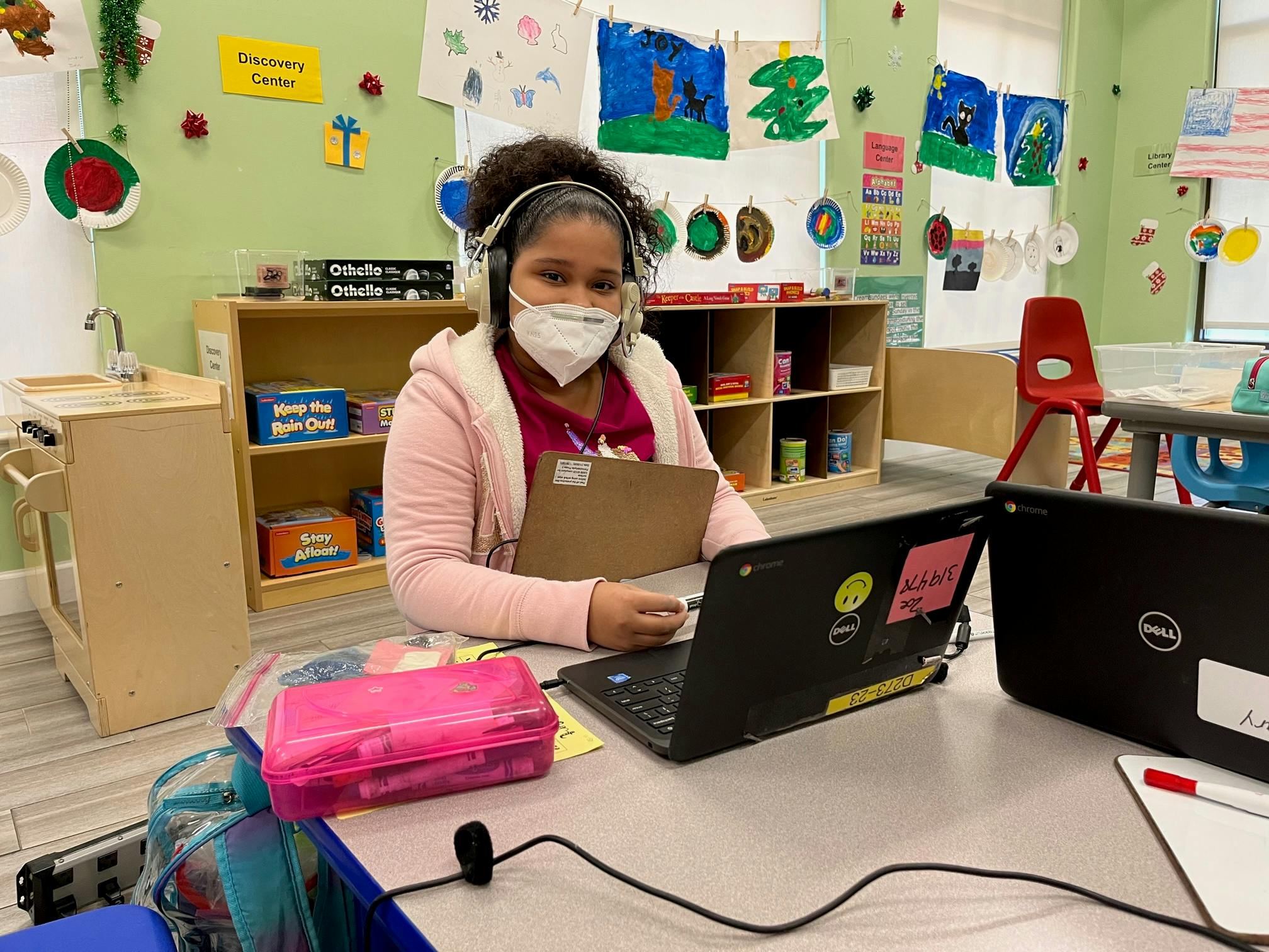 Child in a mask and headphones using a laptop in a classroom