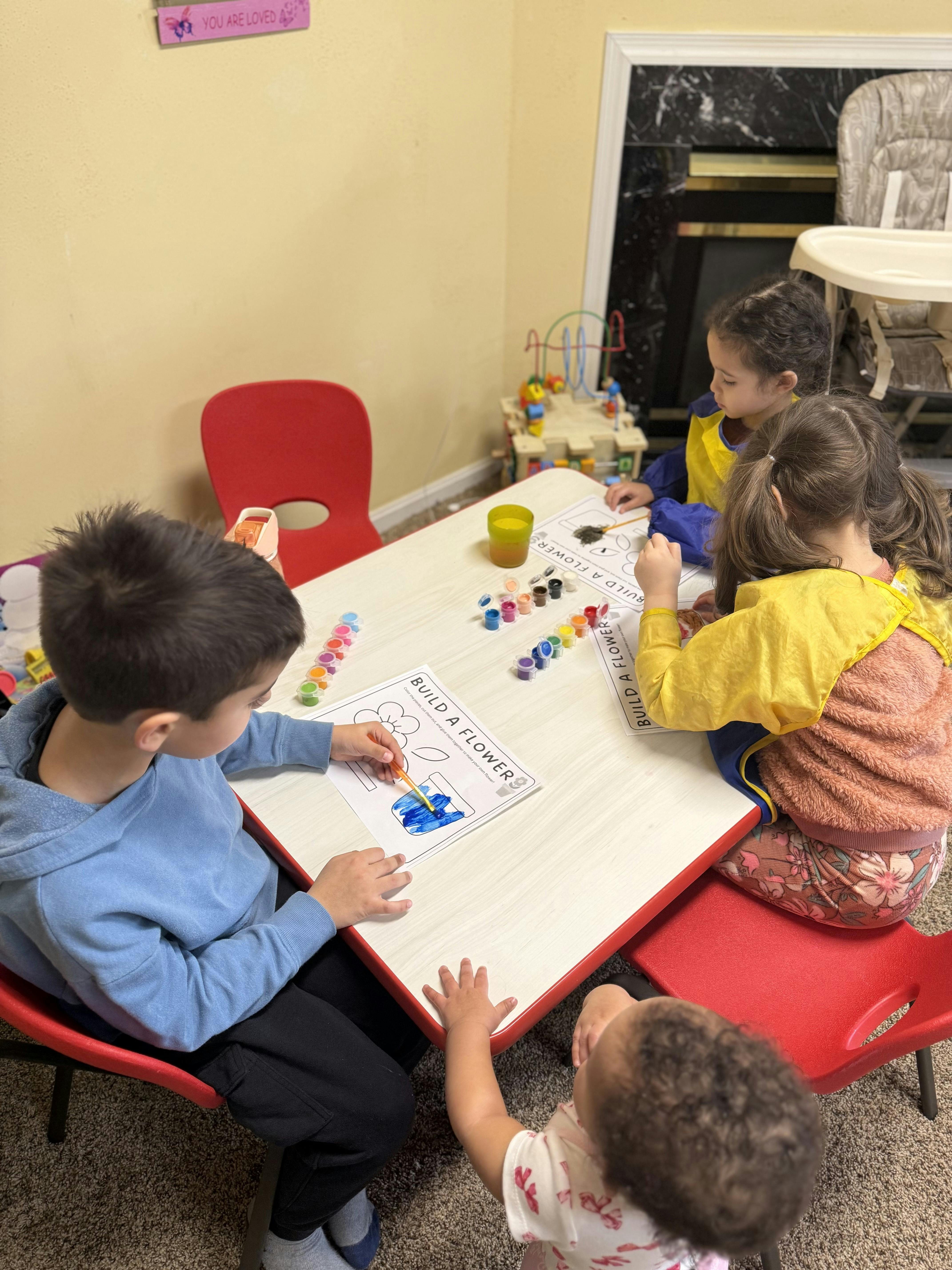 Four children sitting at a table painting flower pictures