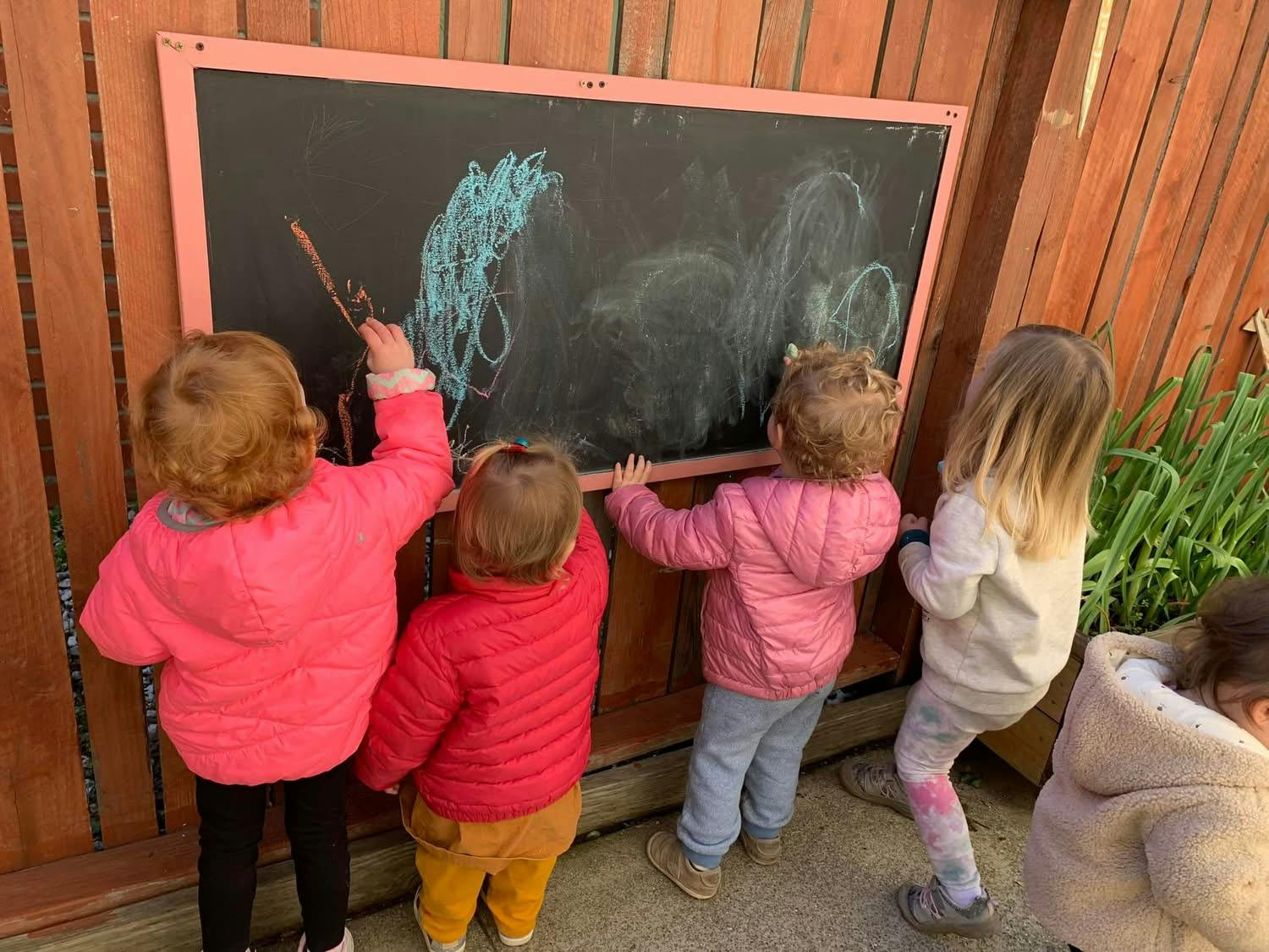 Group of young children drawing with chalk on an outdoor blackboard