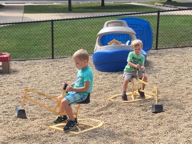 Two children playing on digger toys in a playground