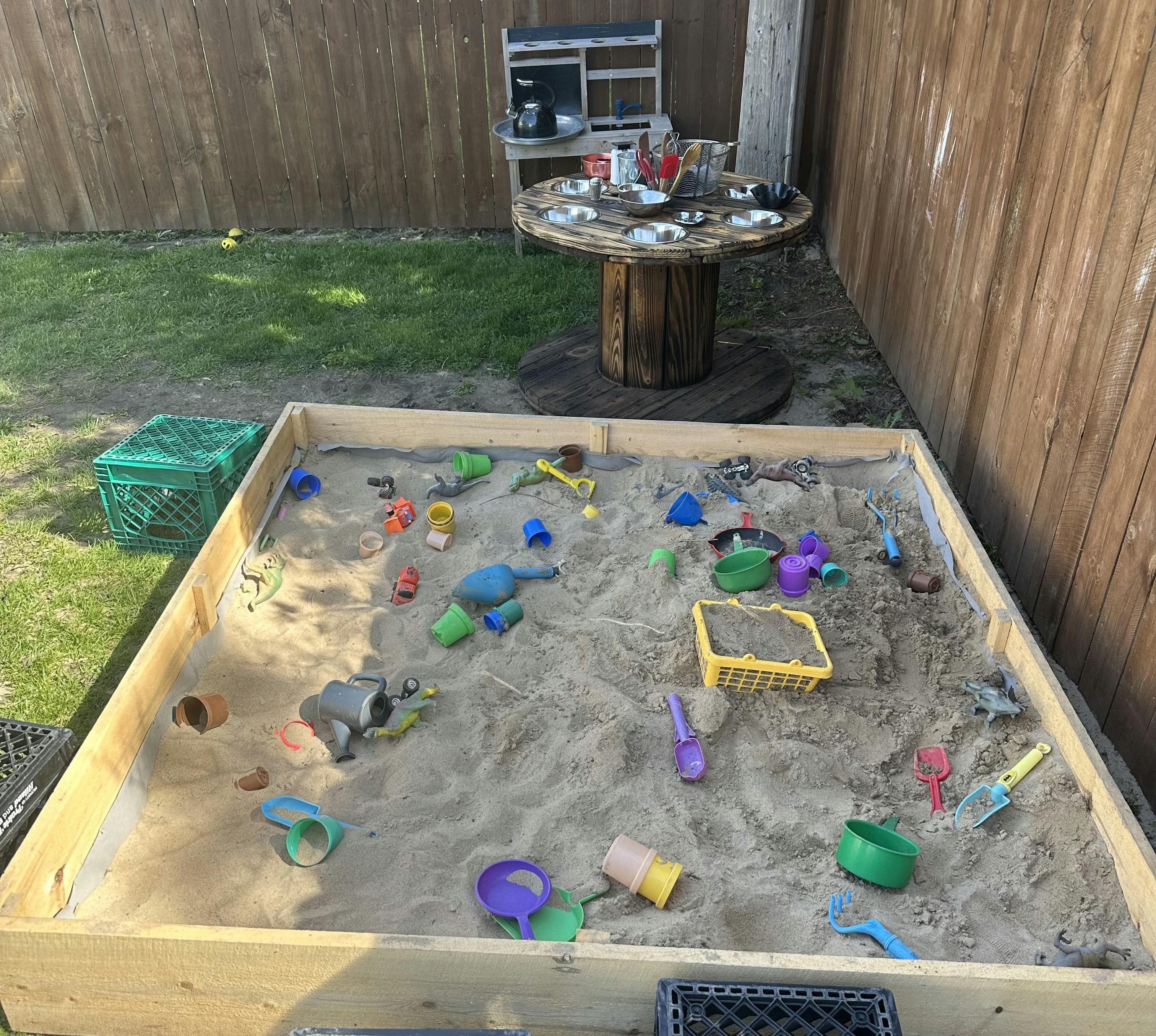 A wooden sandbox filled with sand and various colorful toys