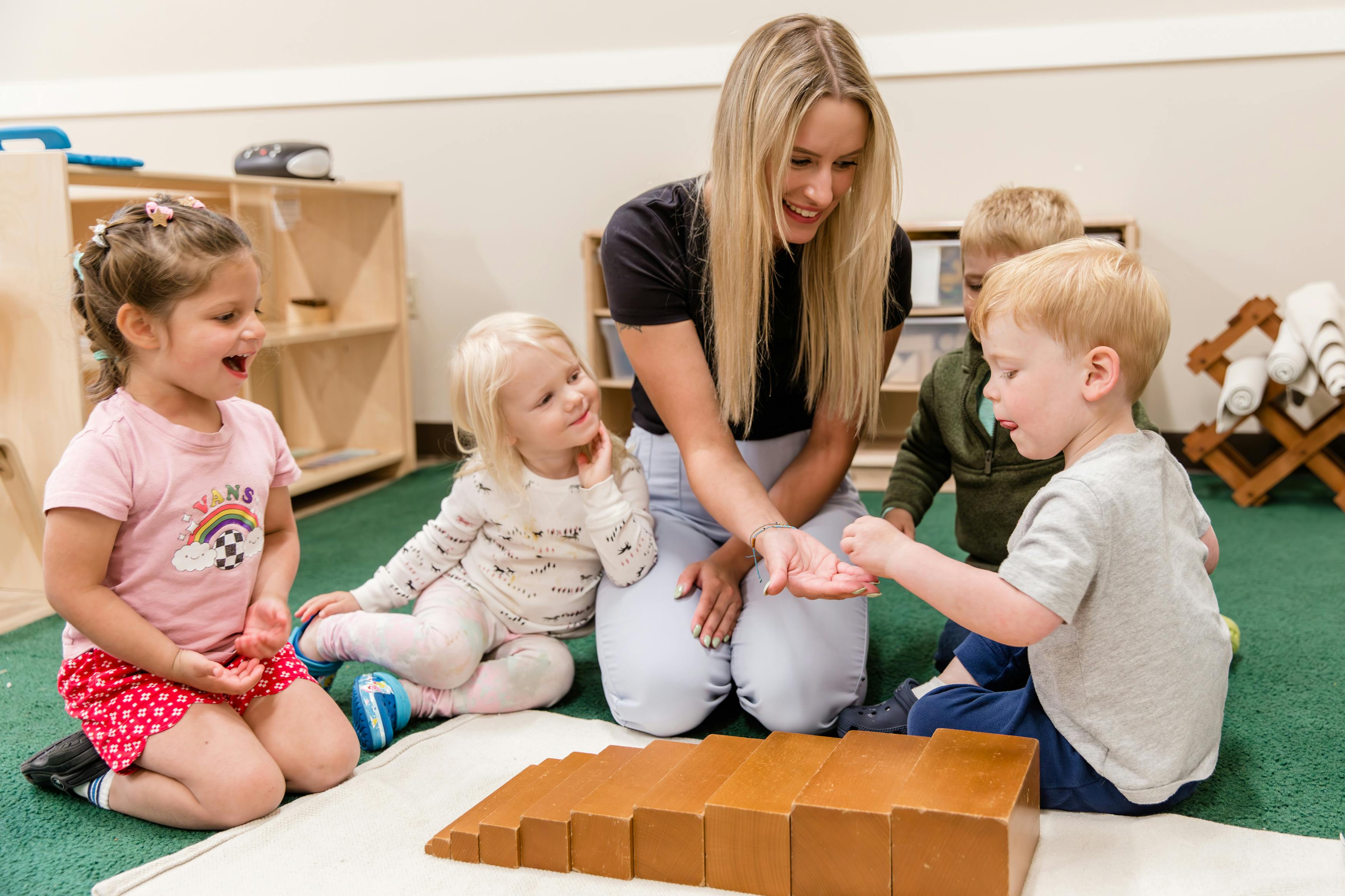Adult and three children on floor playing with wooden blocks