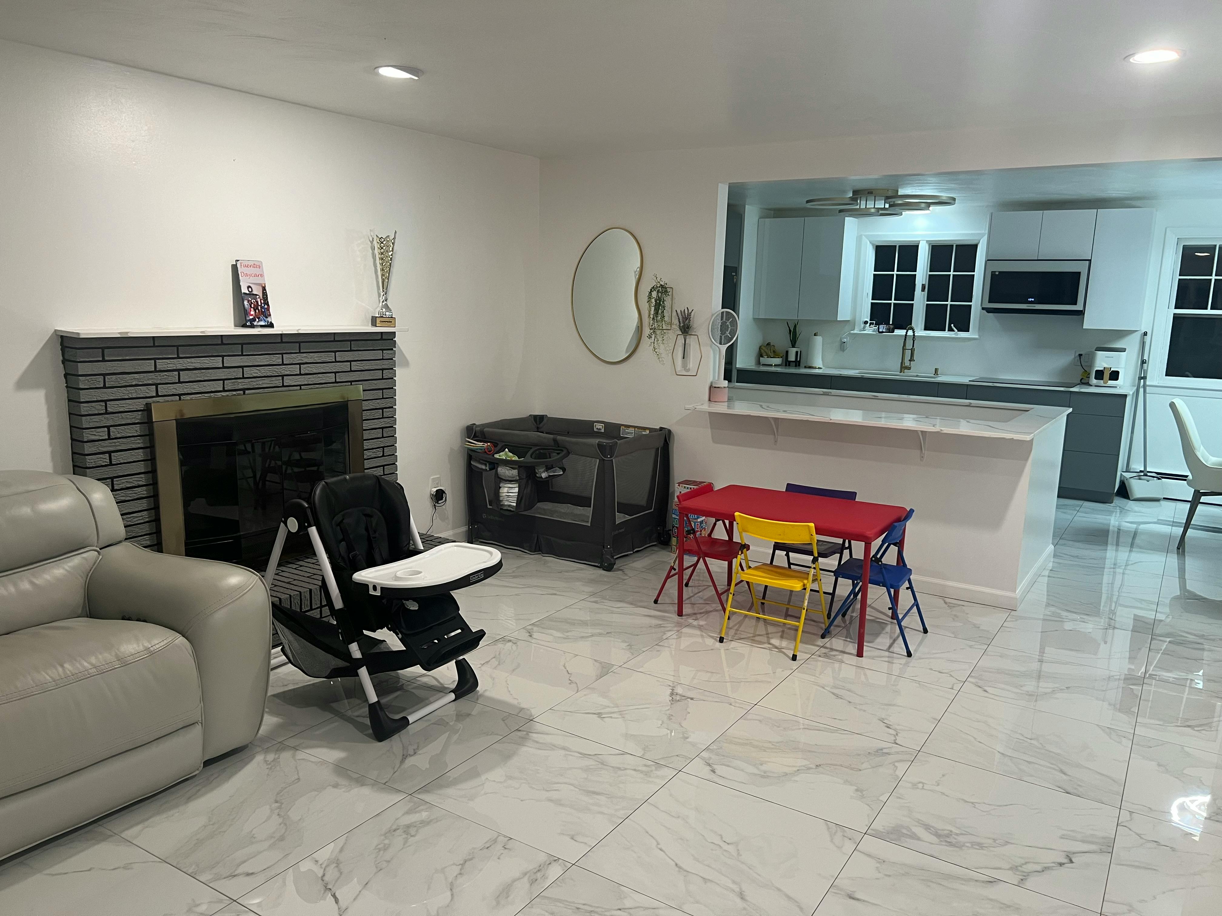 Living room with fireplace, high chair, and children's table, kitchen in background