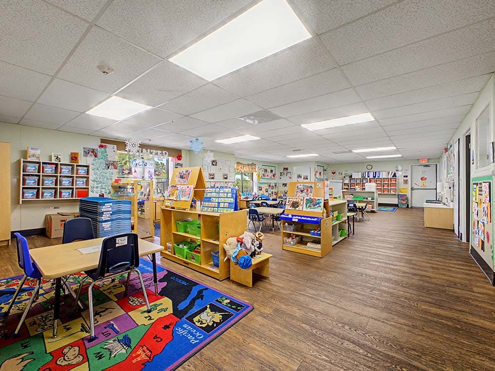 Empty classroom with small tables, chairs, and shelves of educational materials