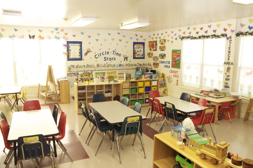 Empty classroom with small tables and chairs, shelves with toys and books