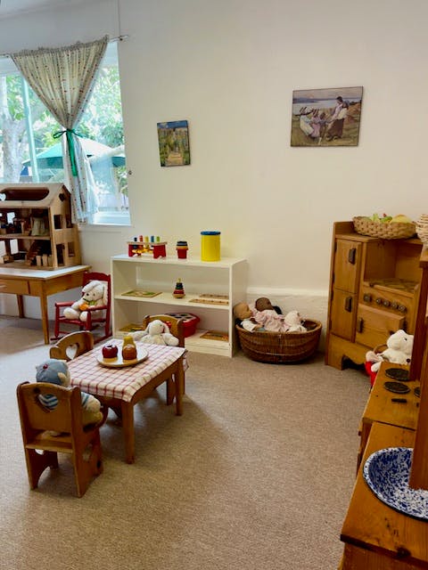 Playroom with small table and chairs, shelves with toys, and dollhouse