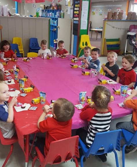 Children sitting at a long table with snacks in a classroom