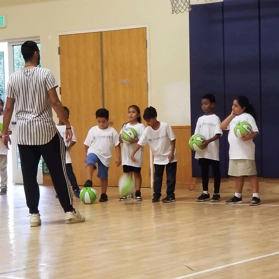 Adult leading children in a gym class with green and white balls