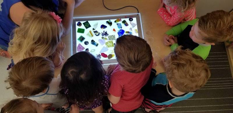 Children gathered around a light table with colorful translucent objects