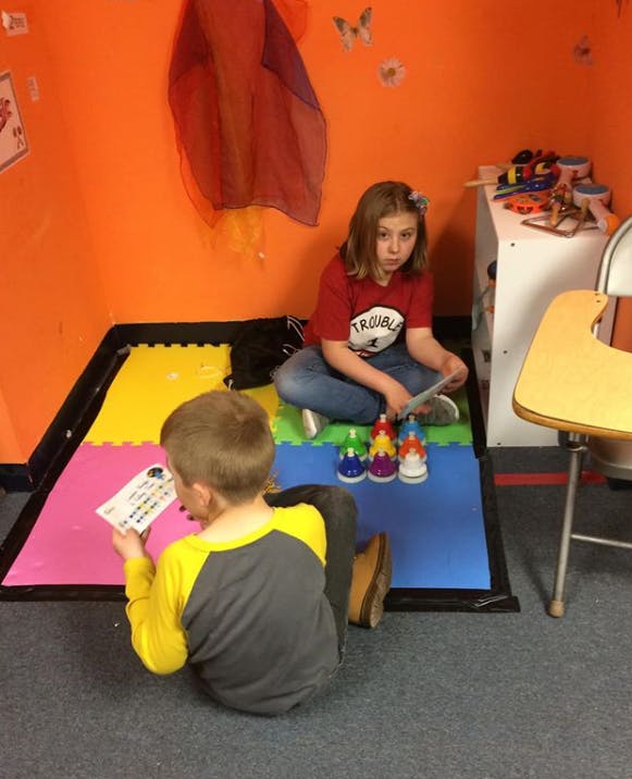 Child reading a card and child sitting with colorful objects on a mat