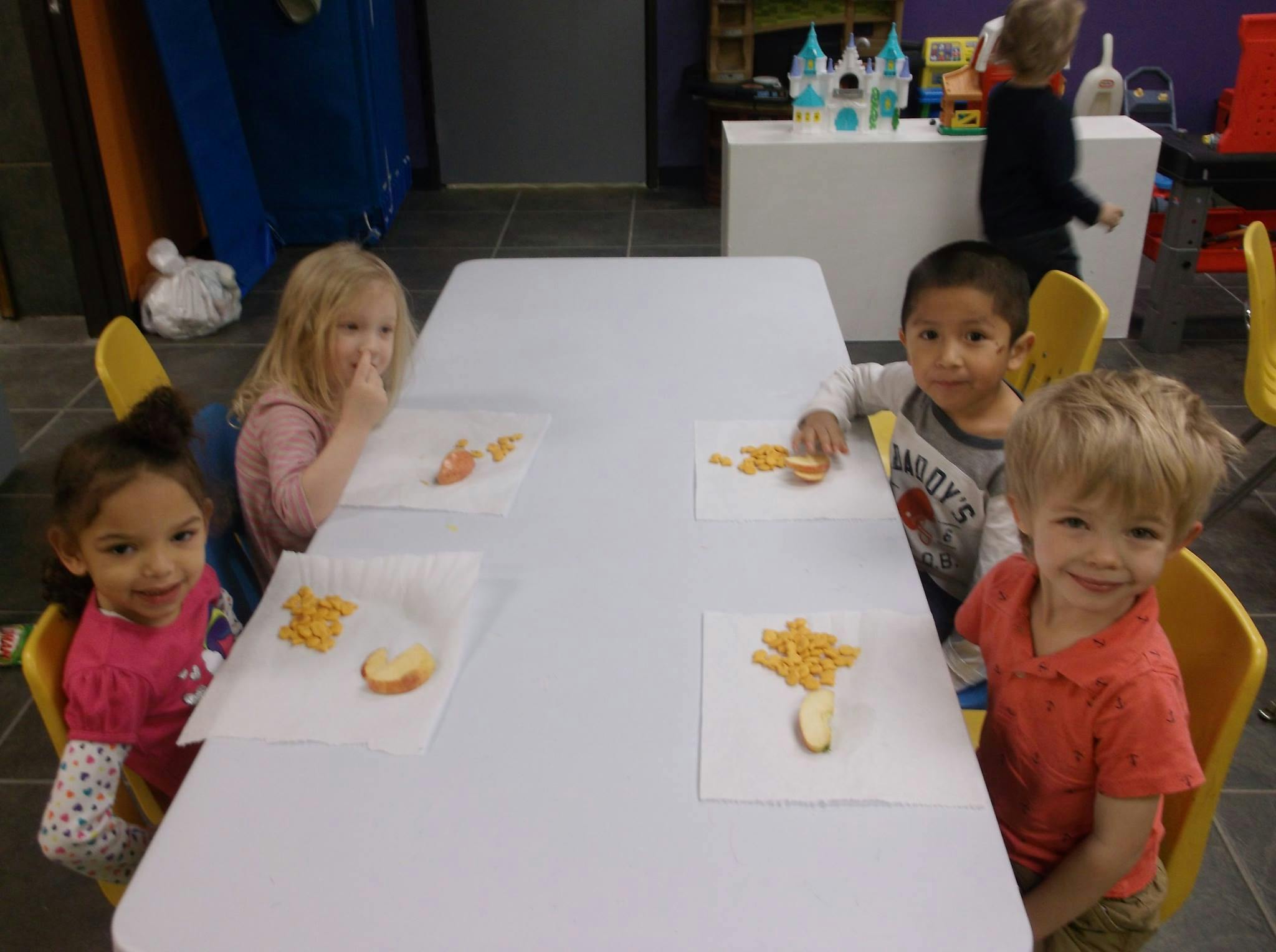 Four children sitting at a table with snacks