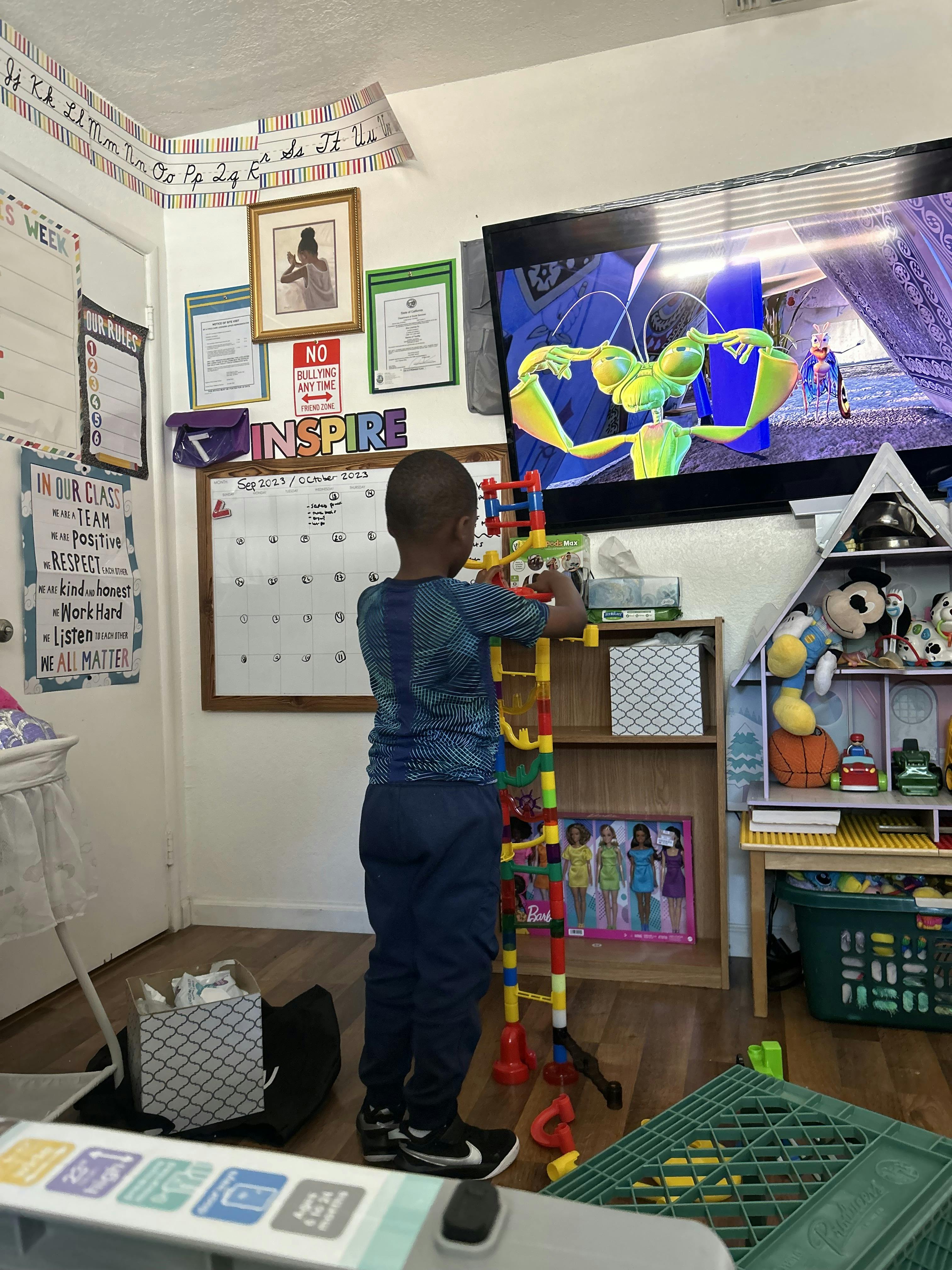 Child standing, playing with a colorful marble run toy in a room with a TV