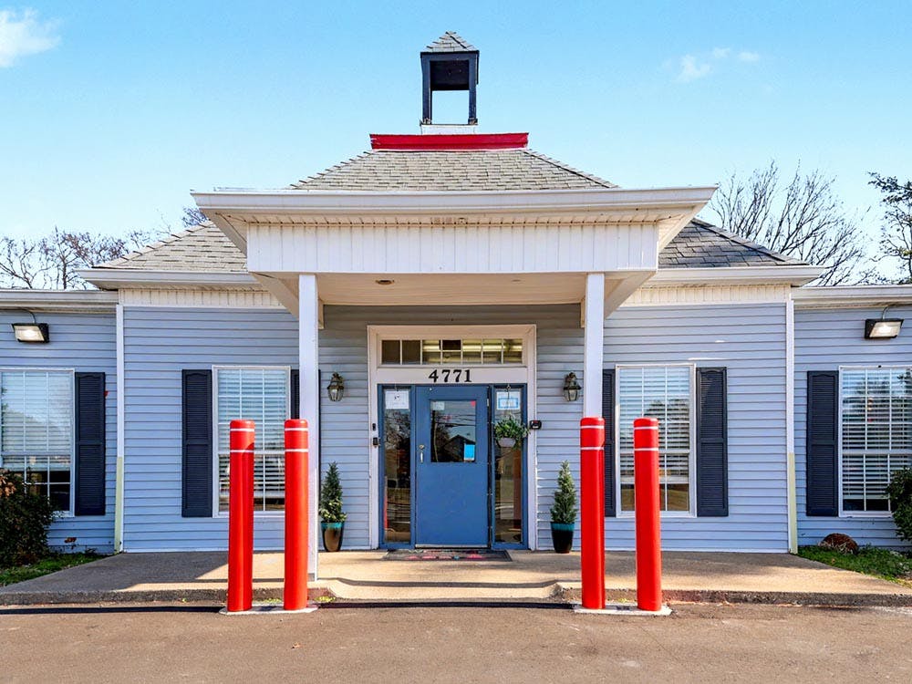 Entrance of a light blue building with a blue door and red bollards