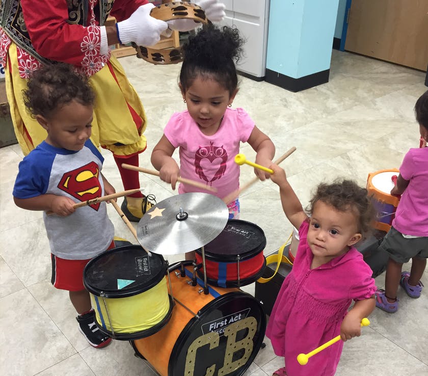 Three children playing with a toy drum set