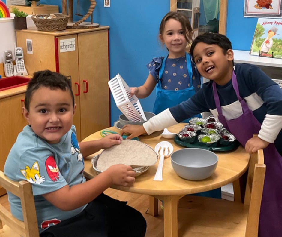 Three children in aprons playing with toy food at a table