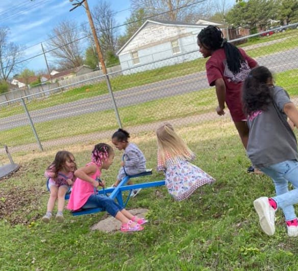 Children playing on a seesaw with adults nearby