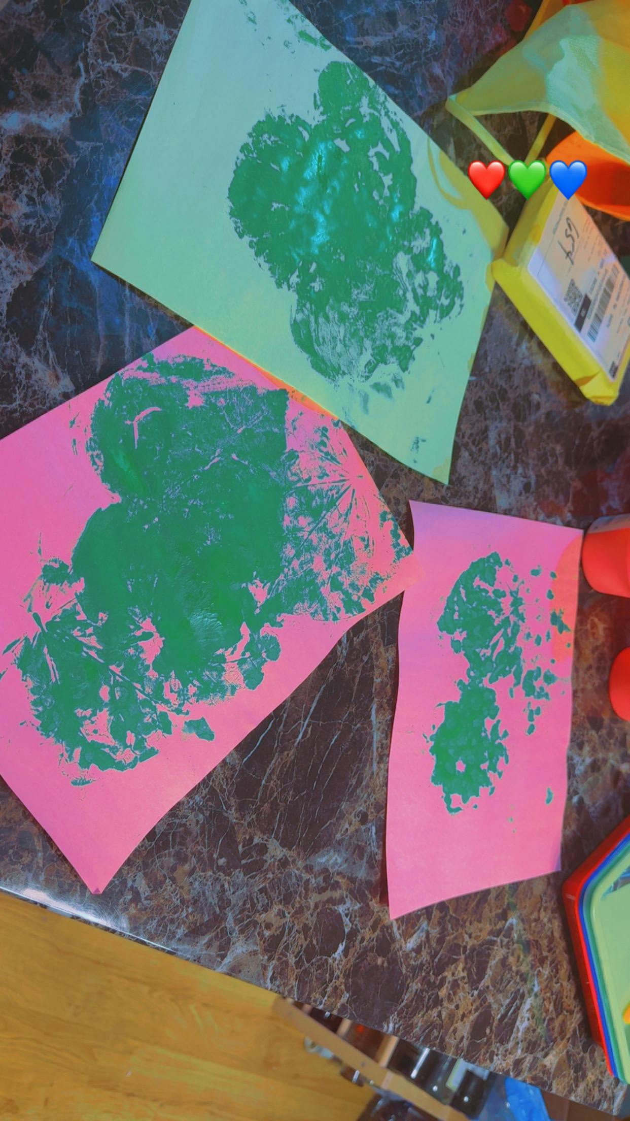 Several pieces of colored paper with green leaf prints on a marble surface