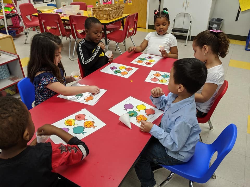 Children sitting at a red table doing an activity with papers