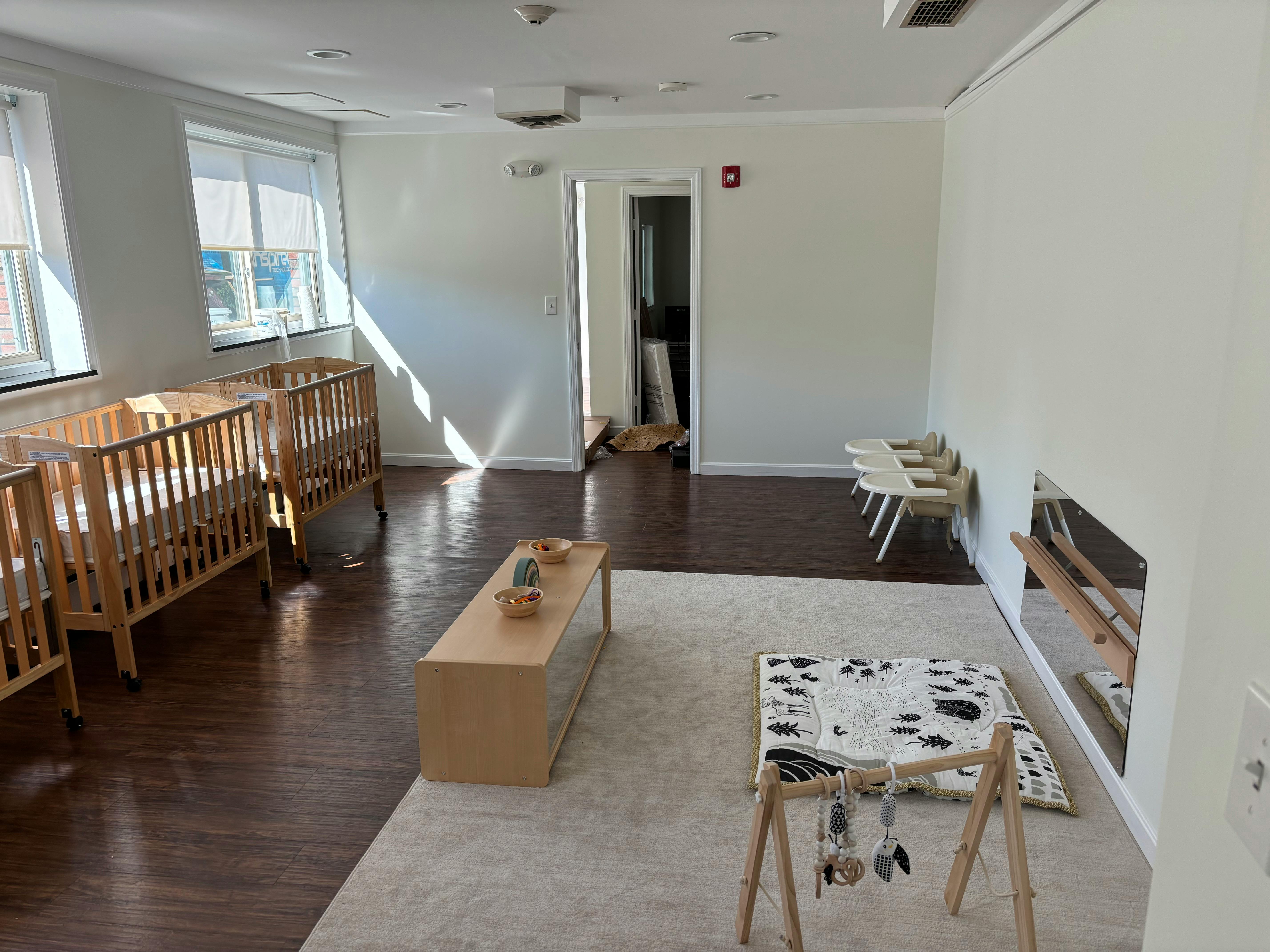 Two wooden cribs in a room with a rug and play mat