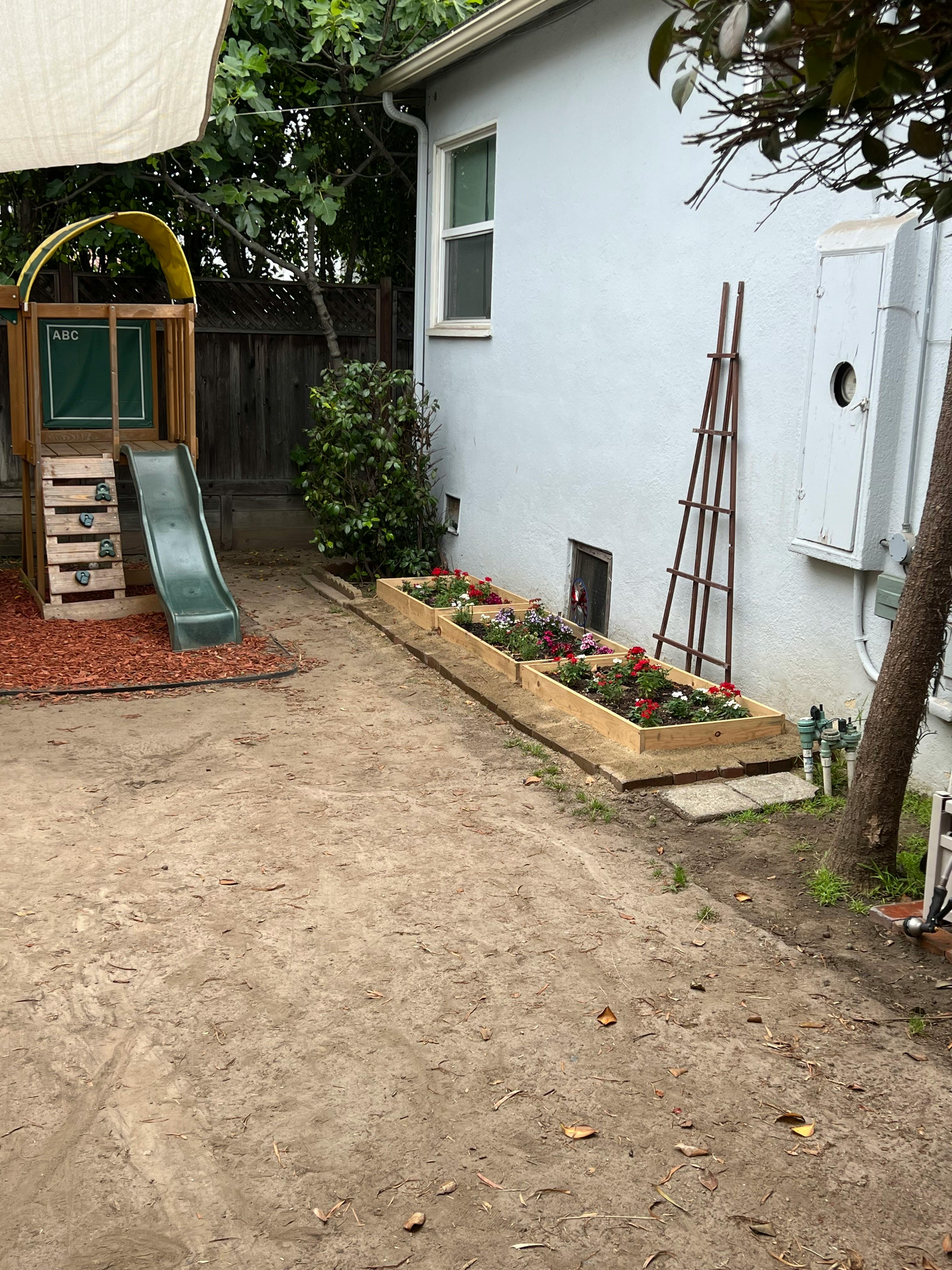 Backyard with a wooden playset and a long planter box with flowers