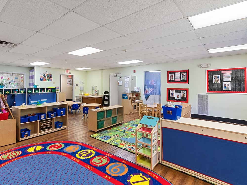 Empty classroom with colorful rugs, shelves, and small tables