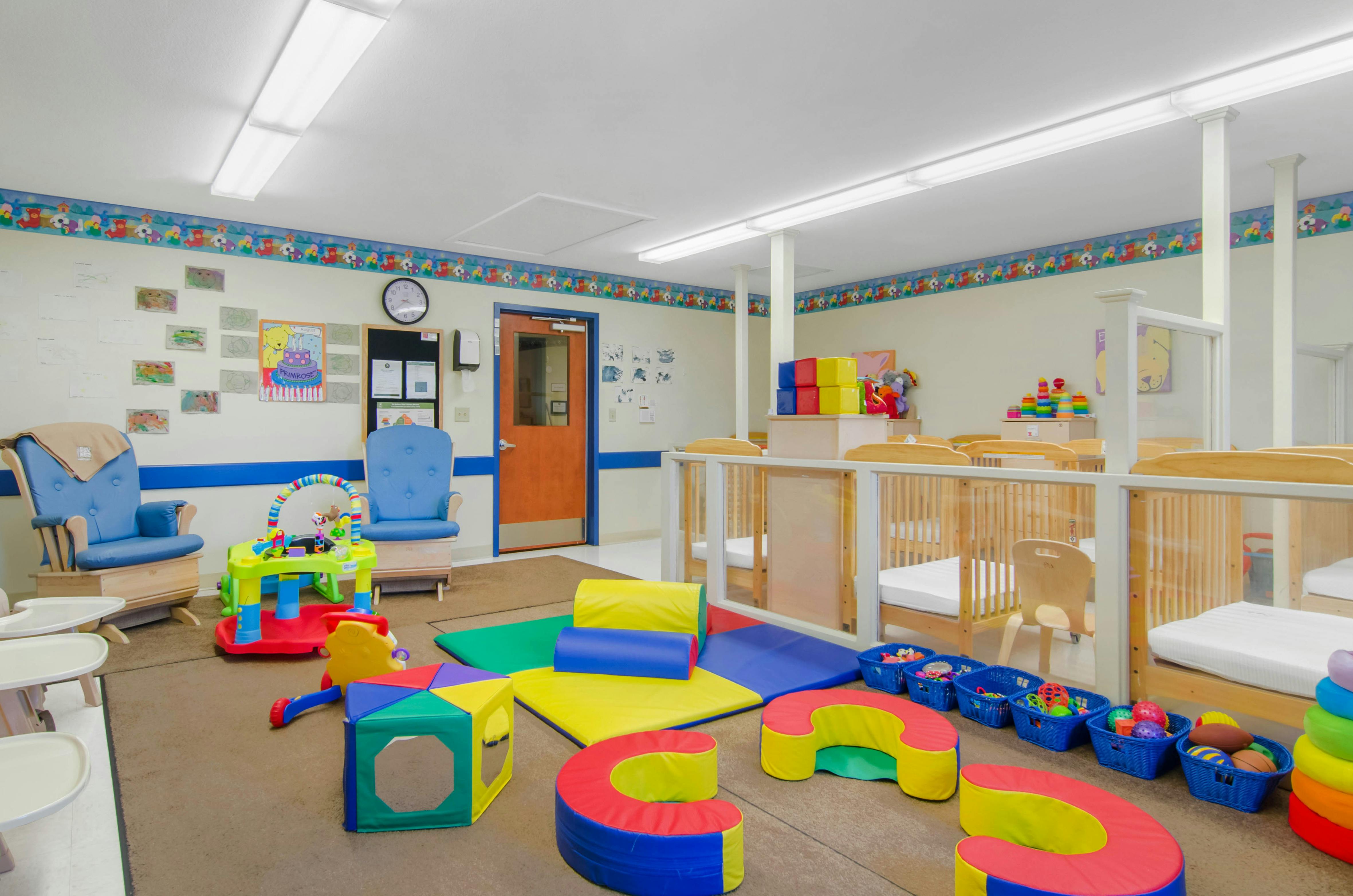 A colorful childcare room with cribs, play mats, and children's furniture