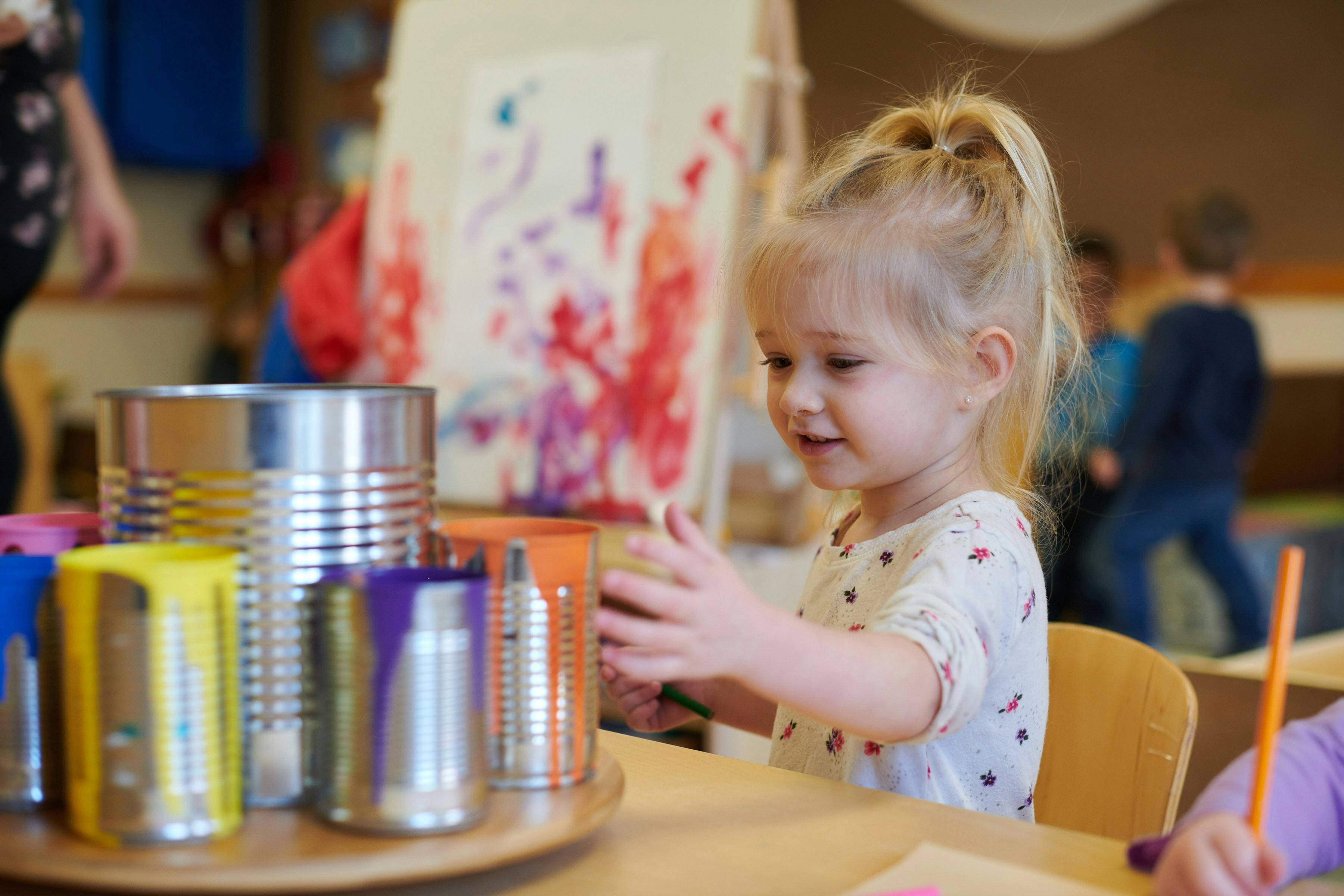 Child sitting at a table with cans, reaching out