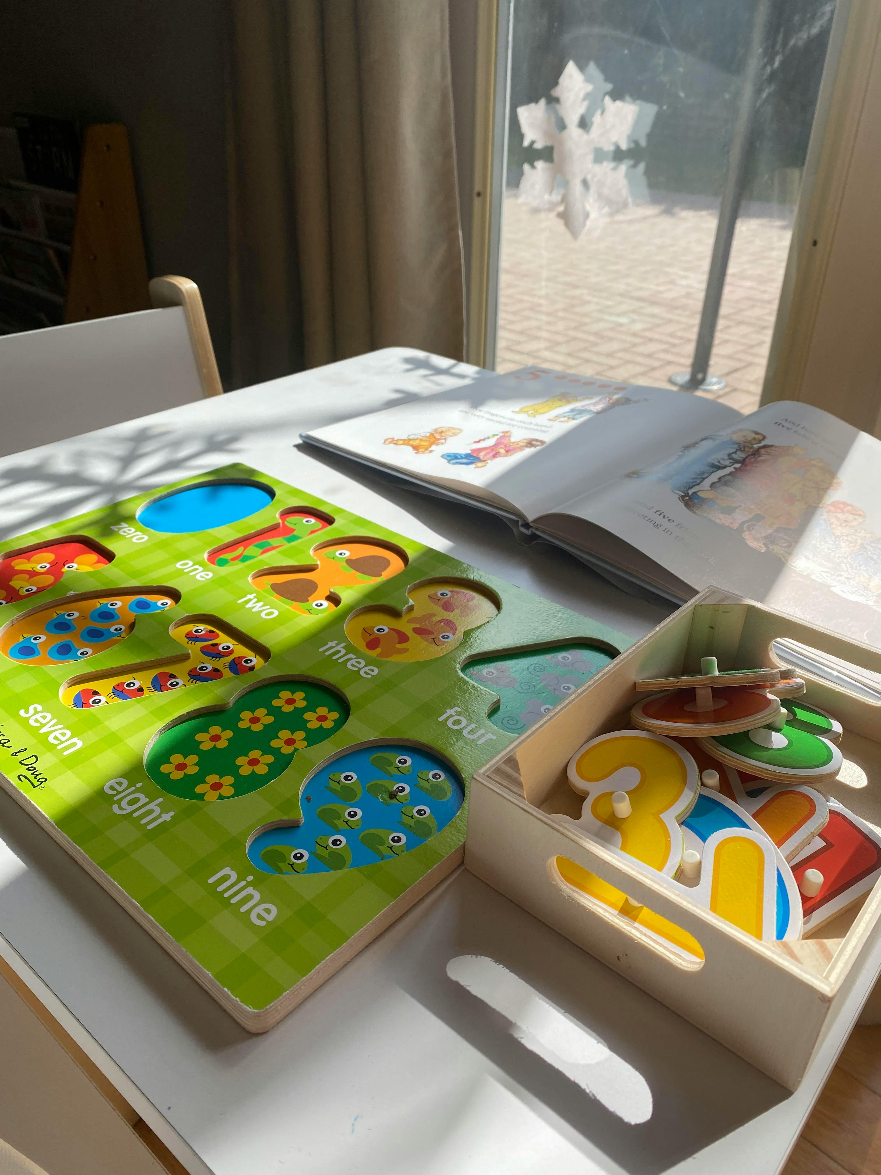 Number puzzle board with pieces removed, open book, and box of puzzle pieces