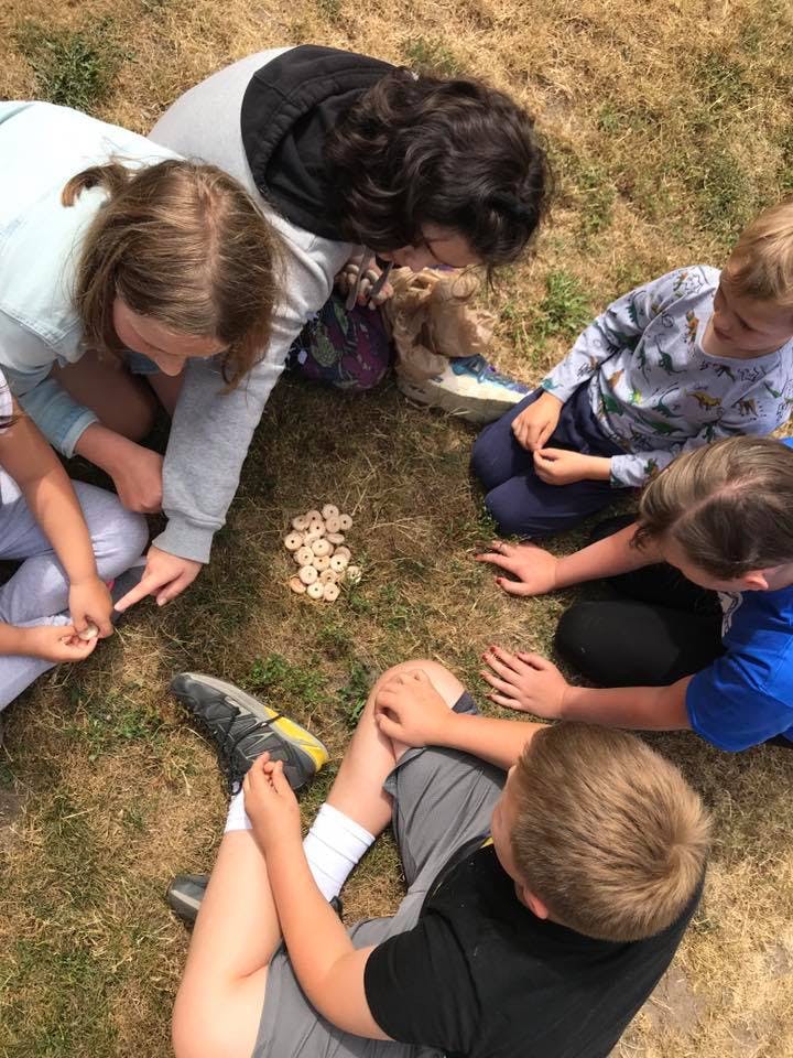 Children gathered around small wooden discs on the ground