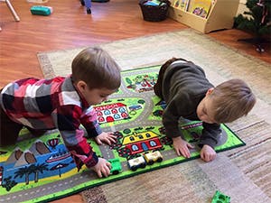 Two children playing with toy cars on a playmat