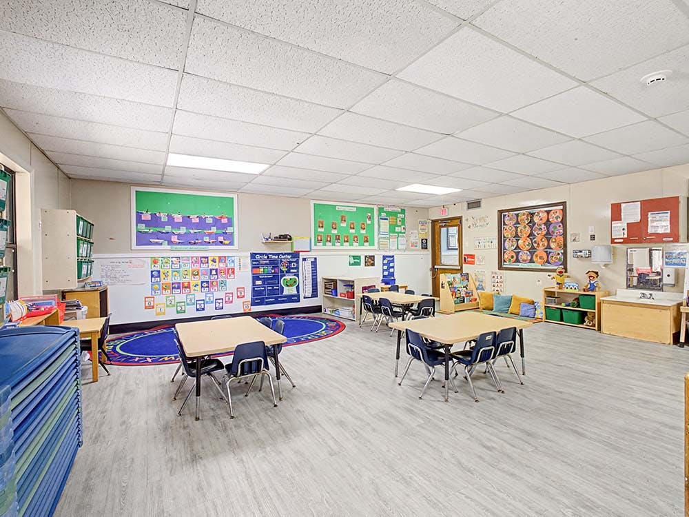 A colorful classroom with small tables, chairs, and learning decorations on the walls