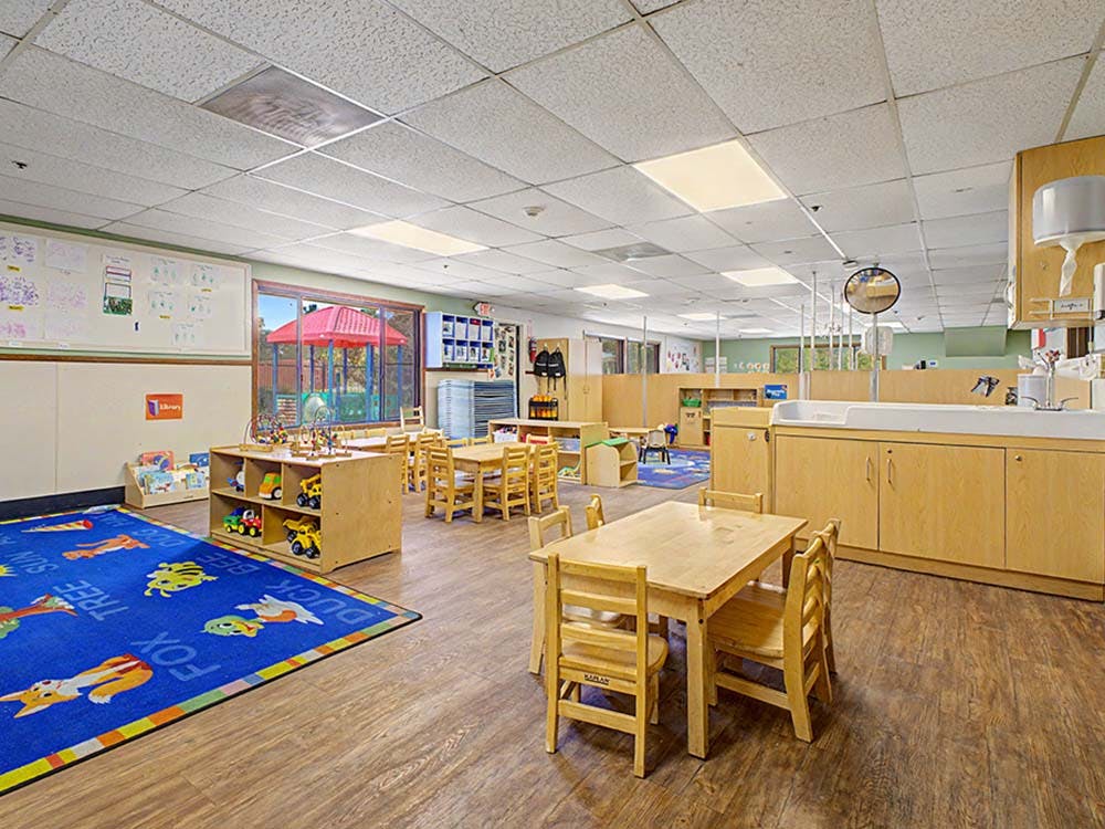 Empty preschool classroom with small tables and chairs and a blue rug