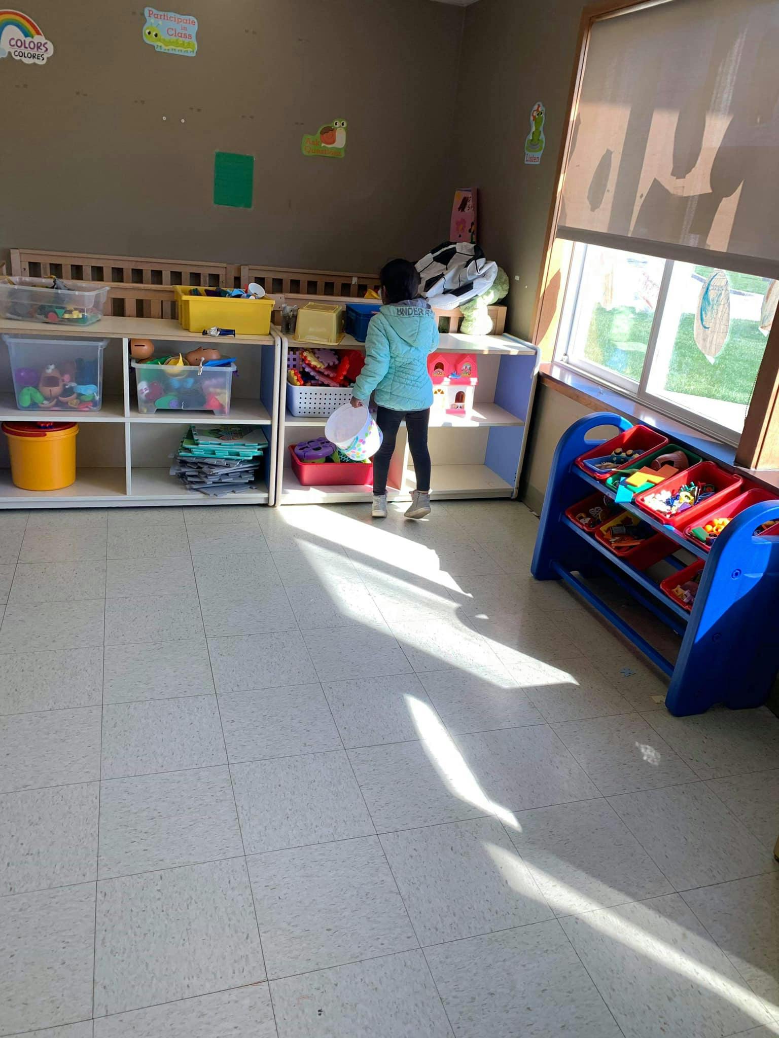 Child standing in a classroom, looking at shelves with toys