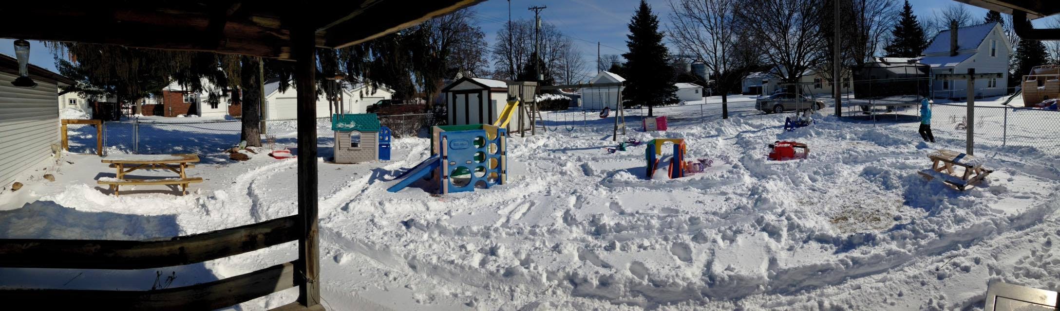 Snow-covered backyard with playground equipment and picnic tables