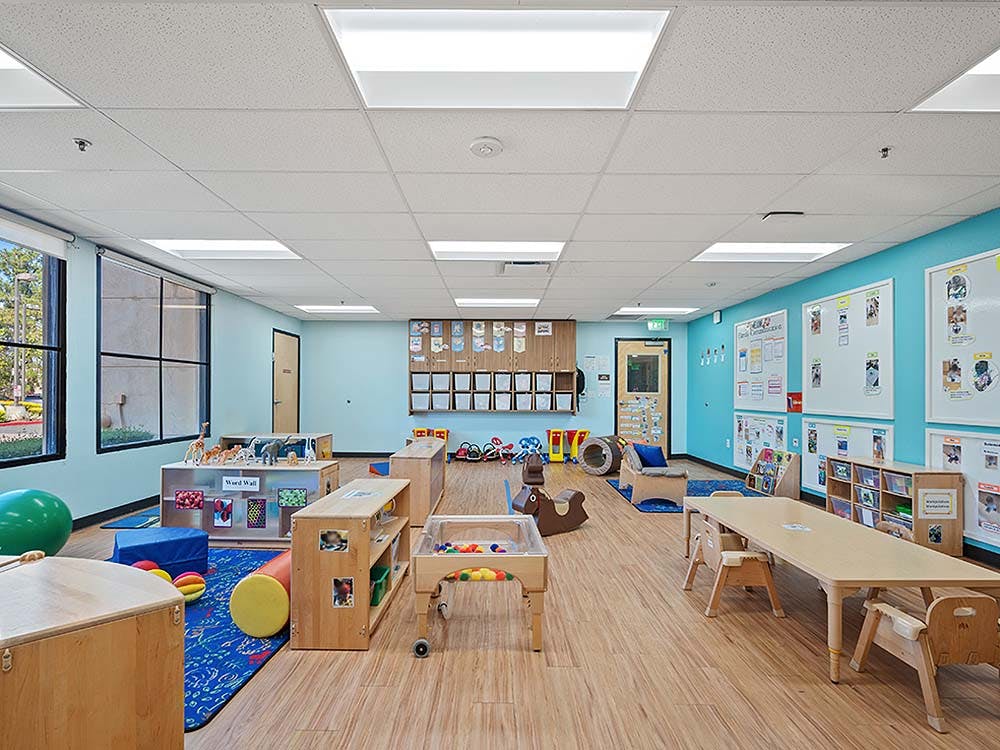Empty colorful preschool classroom with tables, chairs, and play areas