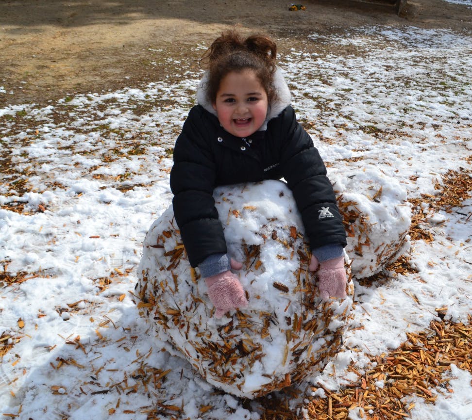 Child in a winter coat leaning on a large snowball