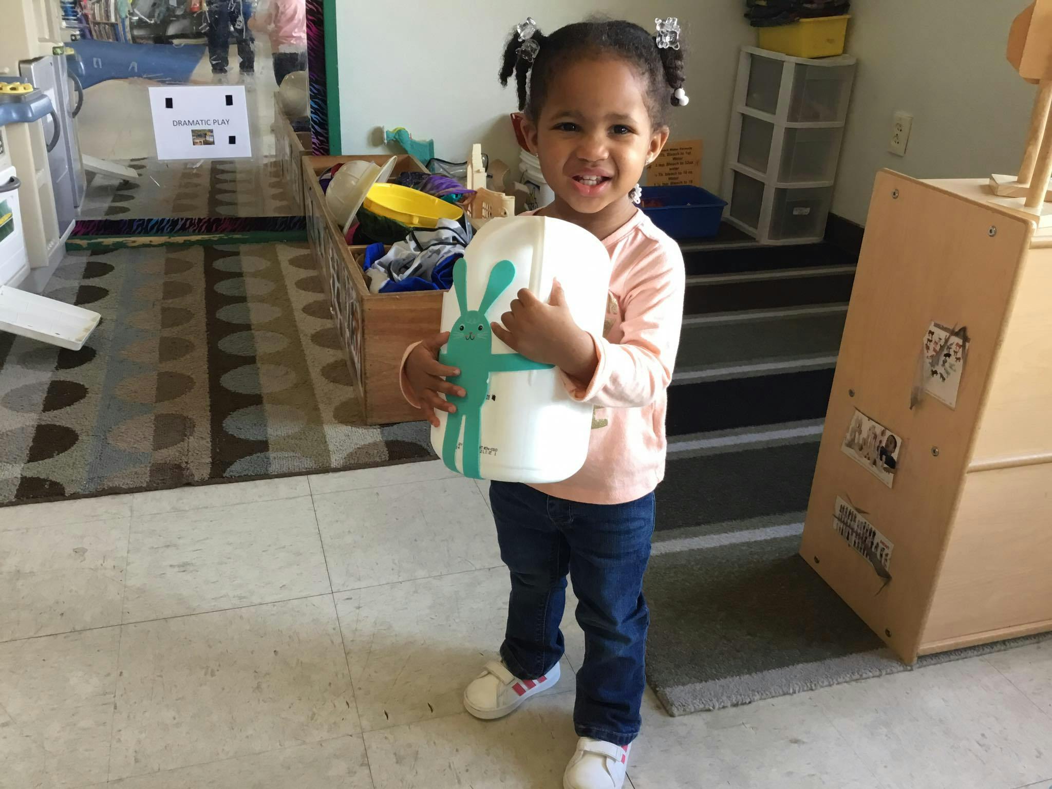 Child holding a large white bottle with a green design