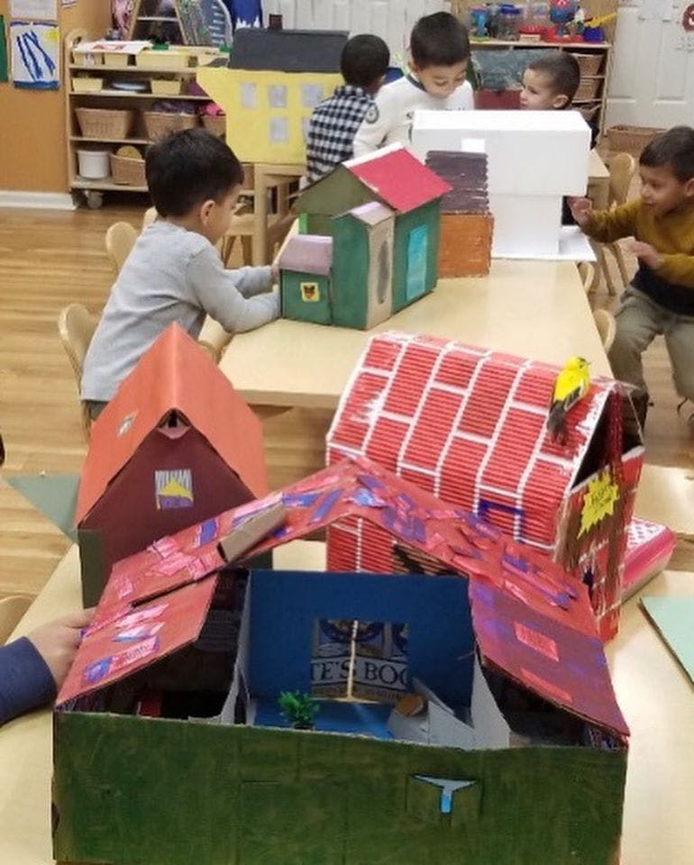 Children playing with cardboard house models in a classroom