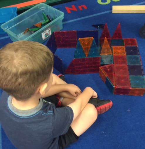 Child sitting on floor playing with magnetic building tiles