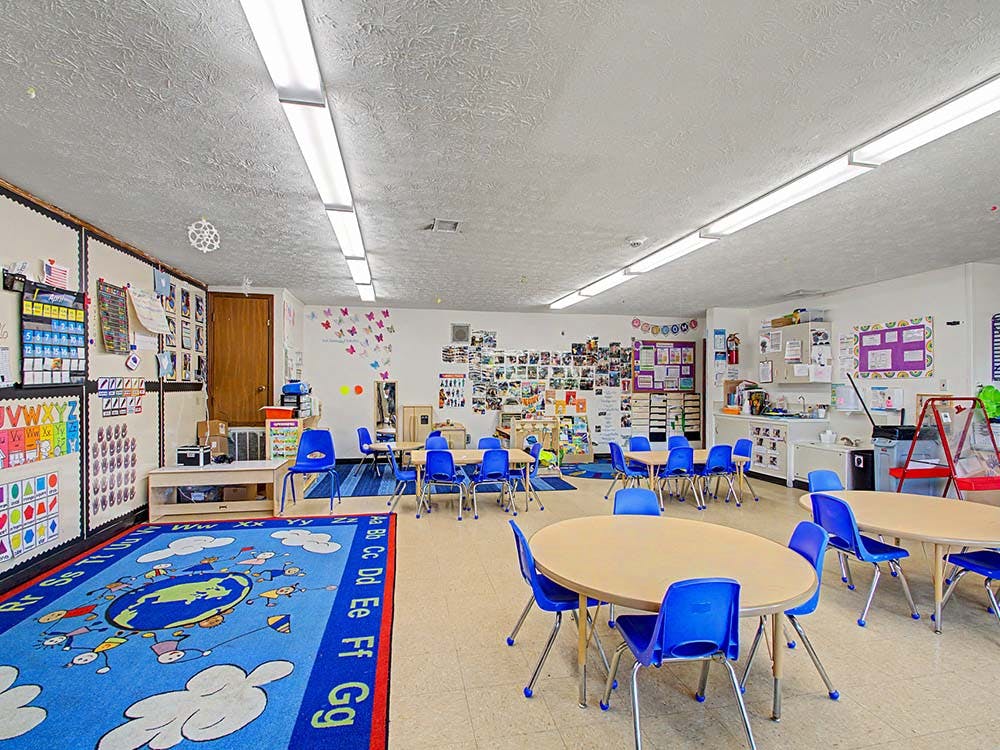 Classroom with small tables, blue chairs, and an alphabet rug