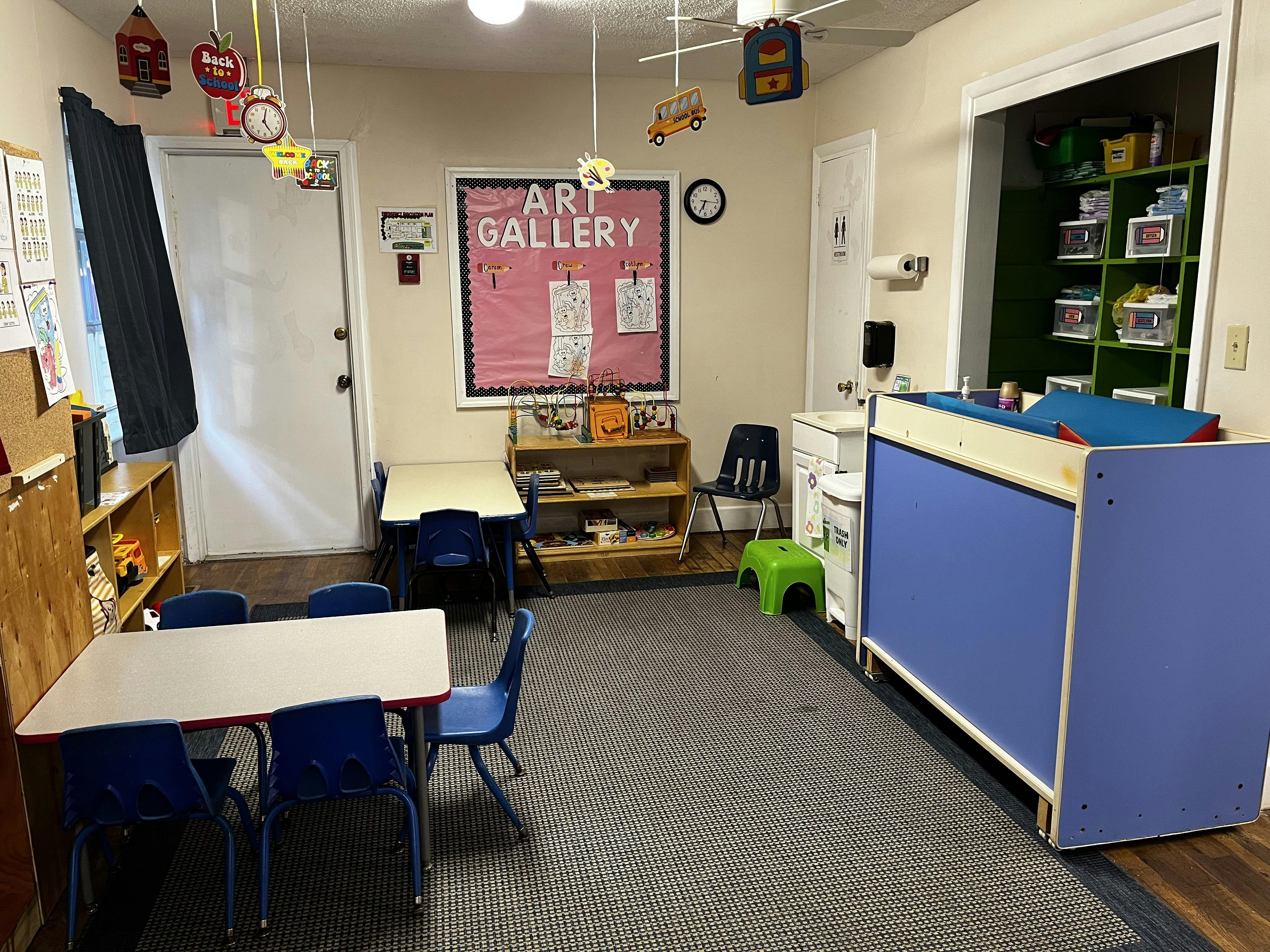 Classroom with small tables and chairs, changing station, and "Art Gallery" sign